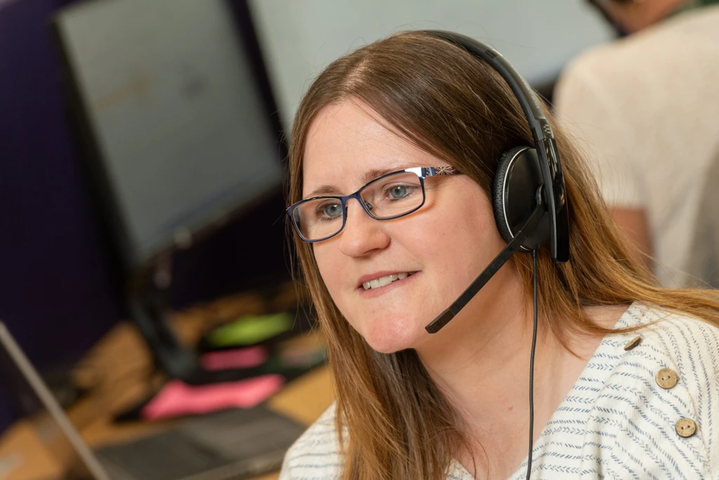 Person wearing glasses and a headset, looking at a computer screen in an office