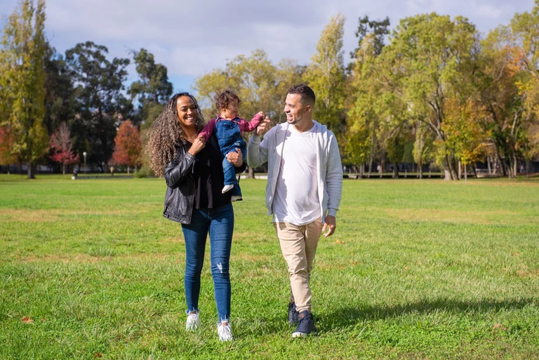 Two adults and a young child walking together across a park with trees in the background