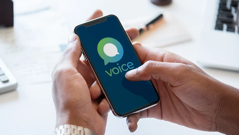 A hand holding a mobile phone showing the Voice logo on screen