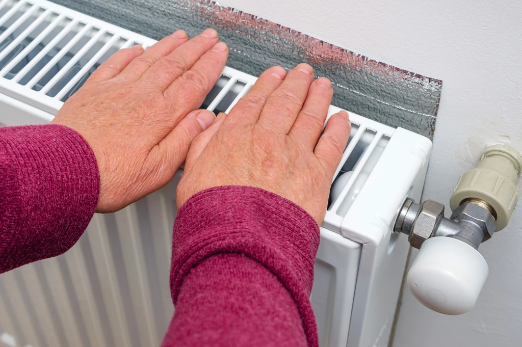 Elderly woman warming her hands on a radiator