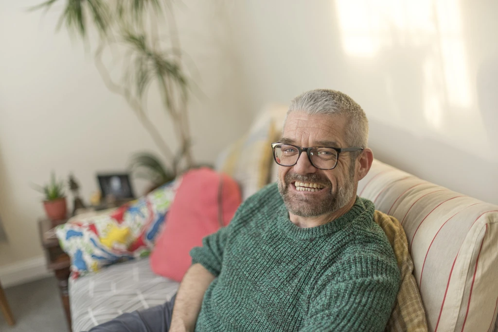 Travis sitting on his sofa, smiling