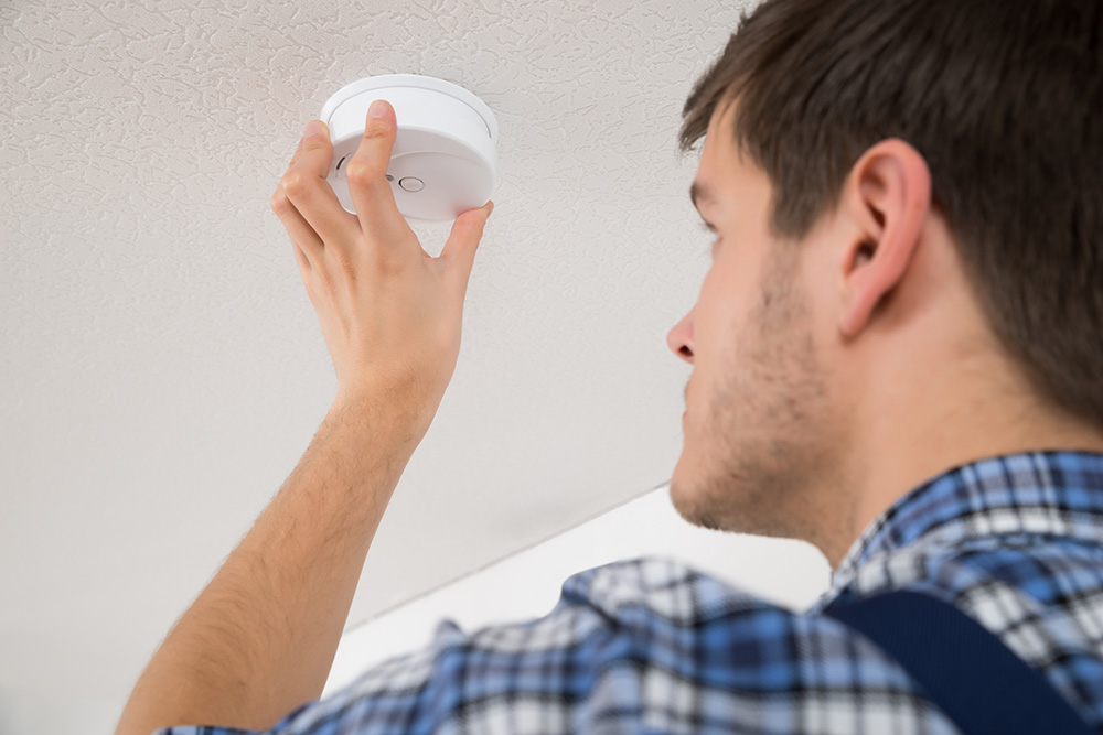 A male tradesman fits a carbon monoxide detector on the ceiling