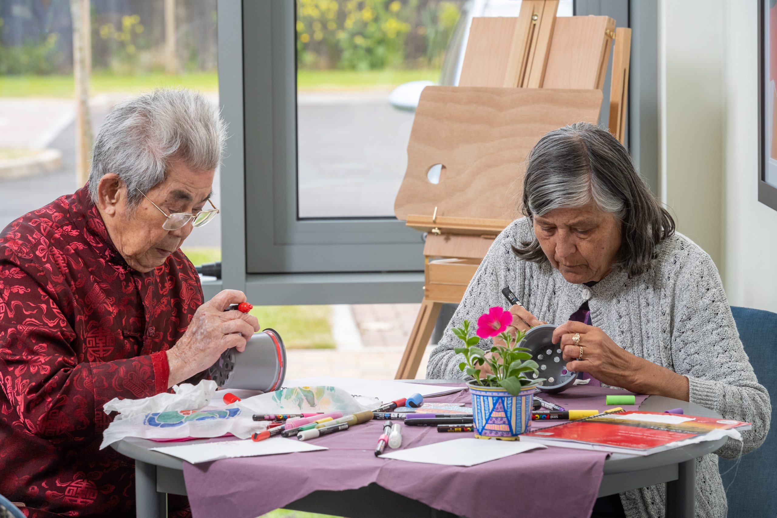 Two people sat a table decorating plant pots in a craft activity session